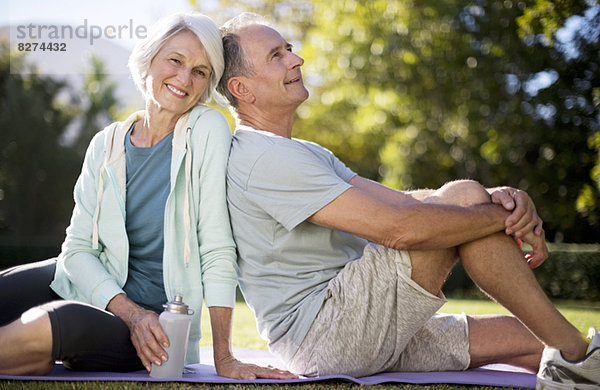 Seniorenpaar sitzend auf Yogamatte im Park