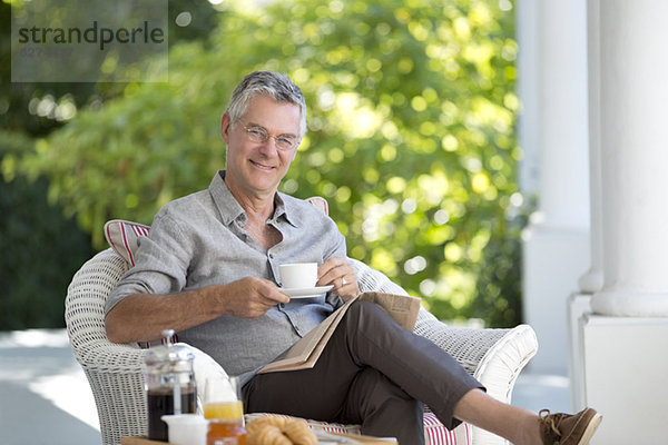 Porträt eines lächelnden älteren Mannes beim Kaffeetrinken auf der Terrasse