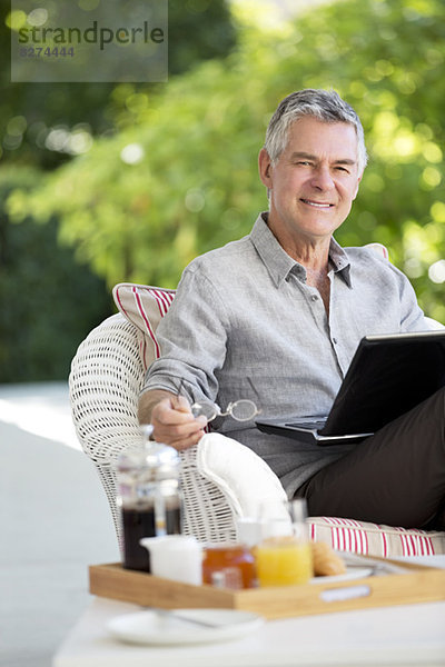 Senior Mann mit Laptop auf der Terrasse