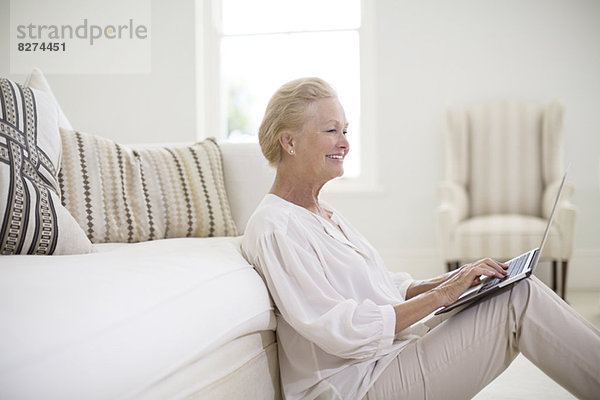 Seniorin mit Laptop auf dem Wohnzimmerboden