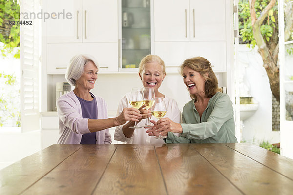 Seniorinnen rösten Weingläser in der Küche.