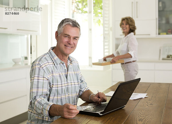 Porträt eines lächelnden älteren Mannes mit Laptop in der Küche