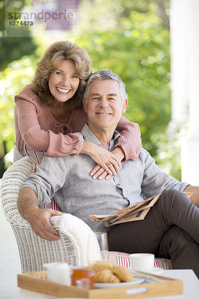 Porträt eines lächelnden älteren Paares  das sich auf der Terrasse umarmt.