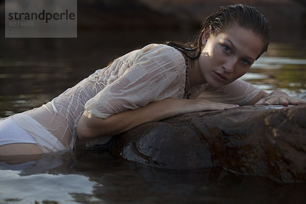 Portrait einer sinnlichen Frau  die auf einem Felsen im Fluss liegt.