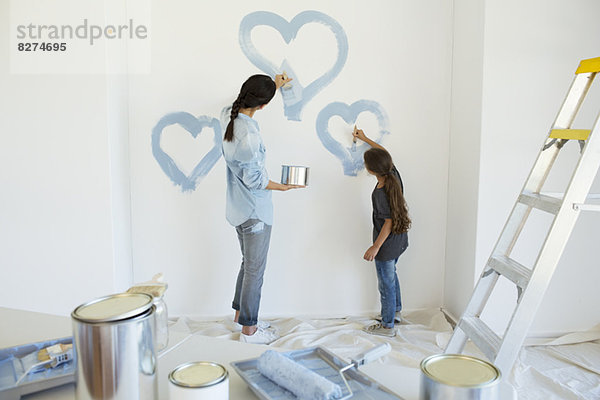 Mutter und Tochter malen blaue Herzen an der Wand im neuen Haus