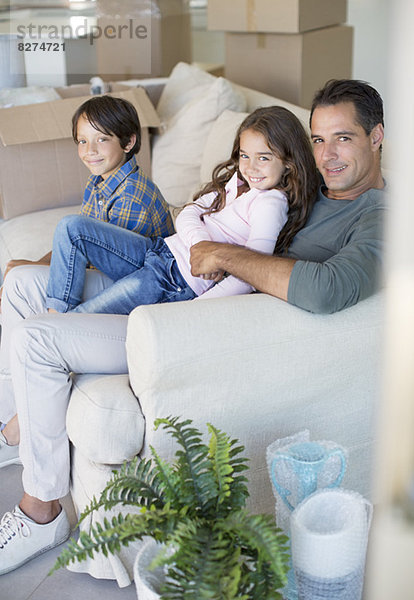 Vater und Kinder entspannen sich auf dem Sofa zwischen Pappkartons