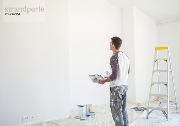 Mann mit Farbwanne mit Blick auf die weiße Wand