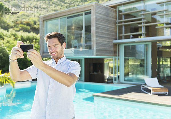 Mann beim Selbstporträt mit Fotohandy am Pool