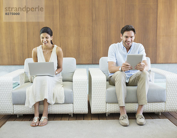 Paar mit Laptop und digitalem Tablett in Sesseln