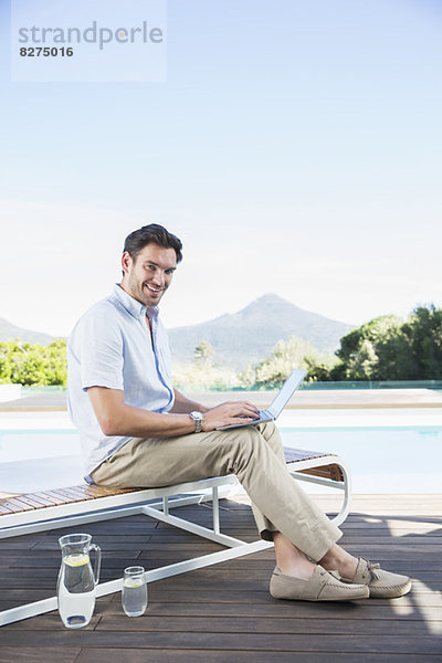 Mann mit Laptop auf dem Sessel am Pool