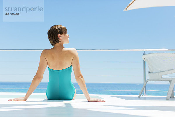 Frau entspannt am Pool mit Meer im Hintergrund