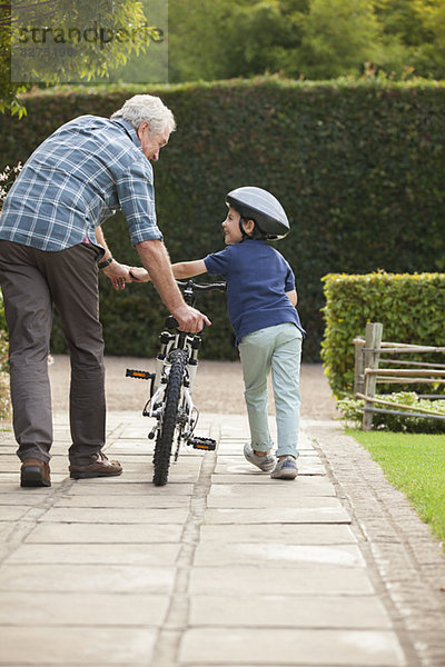 Großvater und Enkel schieben Fahrrad auf Bürgersteig