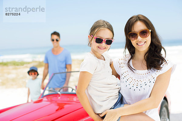 Mutter und Tochter lächeln mit dem Cabrio am Strand