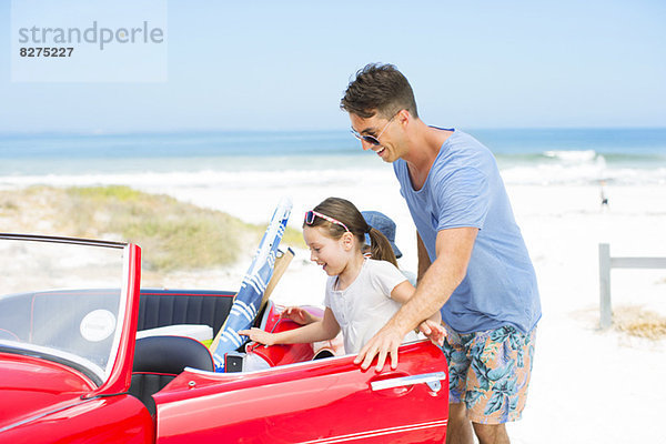 Vater hilft Tochter in Cabrio am Strand