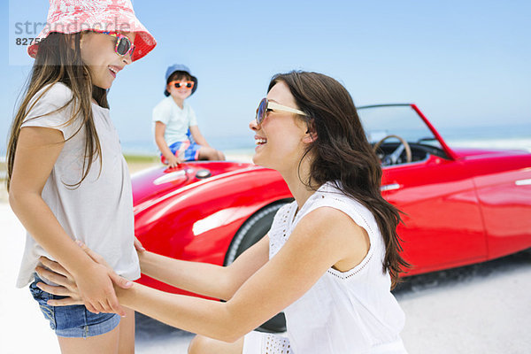 Mutter und Tochter lächeln am Strand beim Cabriolet