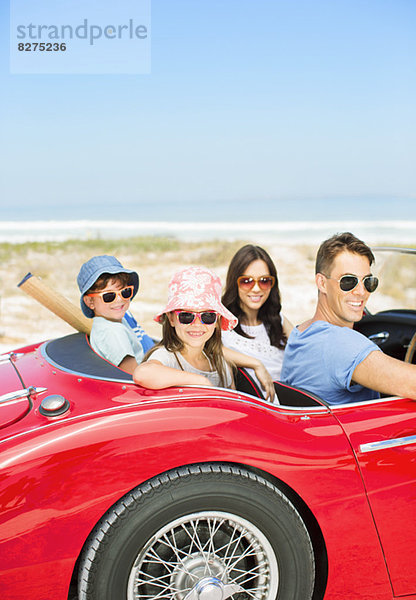 Porträt der lächelnden Familie im Cabrio am Strand