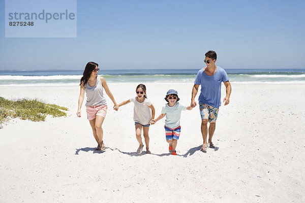 Familie hält sich an den Händen und geht am Strand spazieren