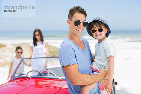 Vater und Sohn lächeln in der Nähe des Cabrios am Strand