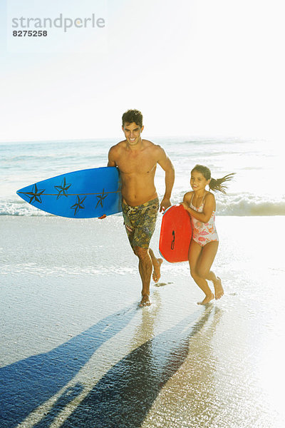 Vater und Tochter mit Surfbrett und Bodyboard am Strand