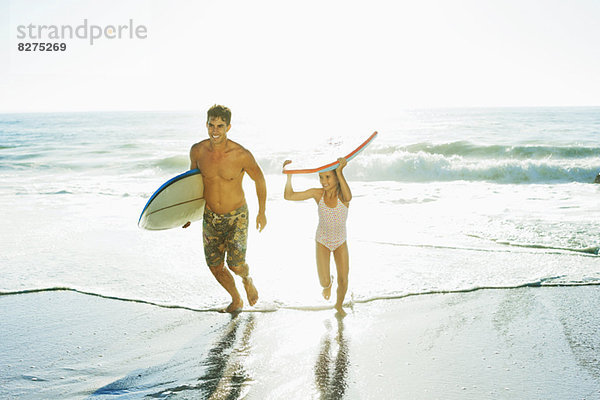 Vater und Tochter mit Surfbrett und Bodyboard am Strand