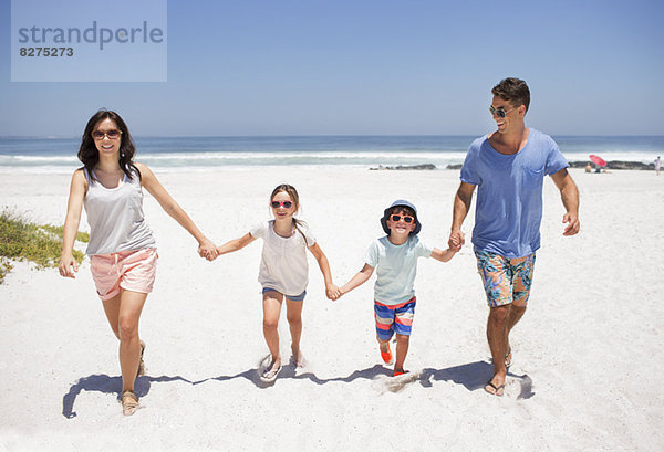 Familie hält sich an den Händen und geht am Strand spazieren