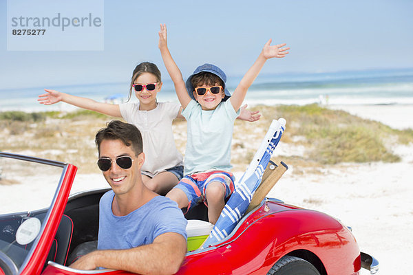 Vater und Kinder lächeln im Cabrio am Strand