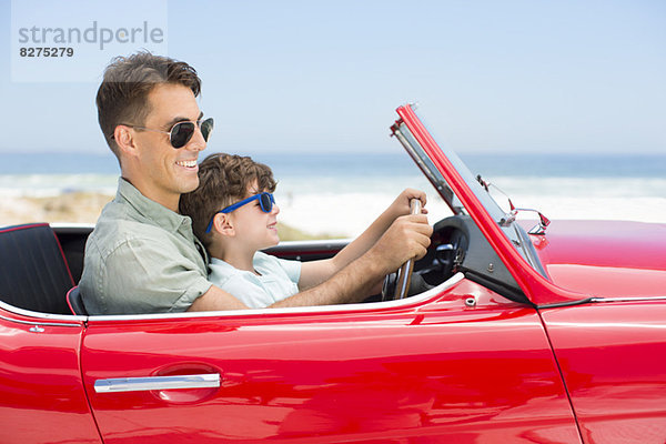 Vater und Sohn fahren Cabrio am Strand