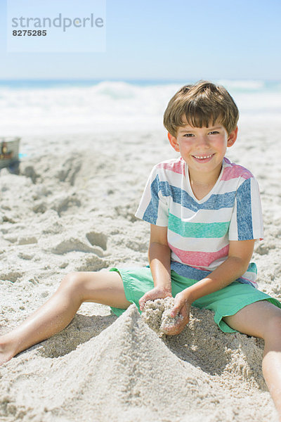 Junge baut Sandburg am Strand