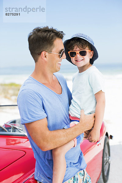 Vater und Sohn lächeln am Strand neben dem Cabriolet