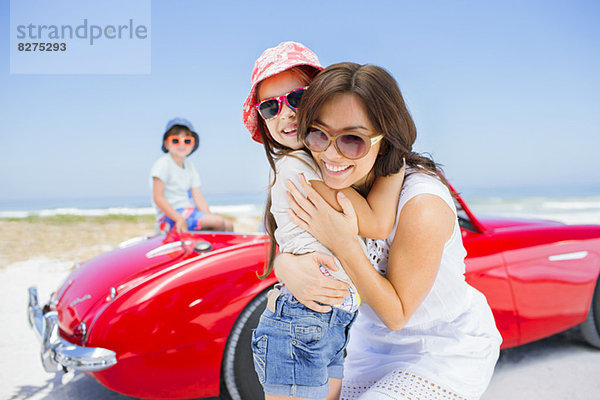 Mutter und Tochter beim Umarmen mit dem Cabrio am Strand