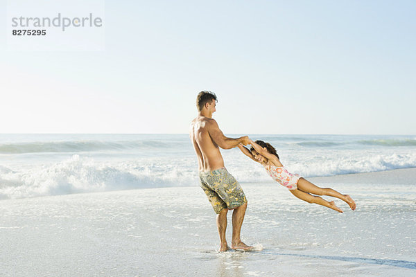 Vater schwingende Tochter beim Surfen am Strand