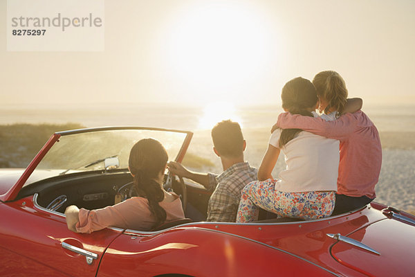 Familie beobachtet Sonnenuntergang über dem Meer vom Cabrio am Strand aus