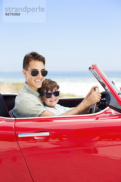 Vater und Sohn fahren Cabrio am Strand