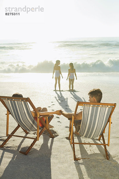 Eltern beobachten Töchter am Strand bei Sonnenuntergang