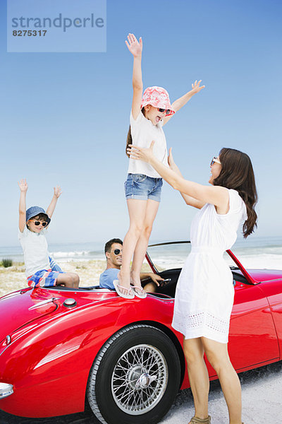 Mädchen  das vom Cabriolet am Strand in die Arme springt.