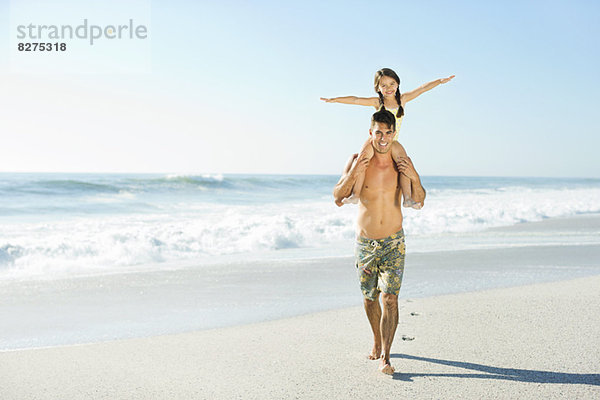 Vater trägt Tochter auf Schultern am Strand