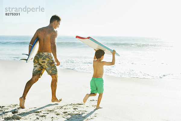 Vater und Sohn mit Surfbrett und Bodyboard am Strand