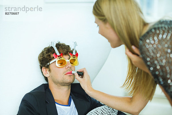 Frau beim Auftragen von Lippenstift auf den schlafenden Mann auf der Party