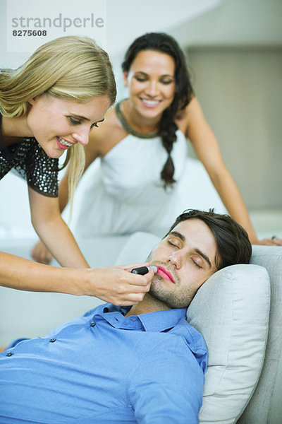 Frau beim Auftragen von Lippenstift auf den schlafenden Mann