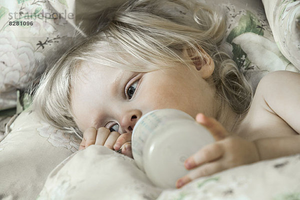 Müde Mädchen auf dem Bett trinken aus der Milchflasche