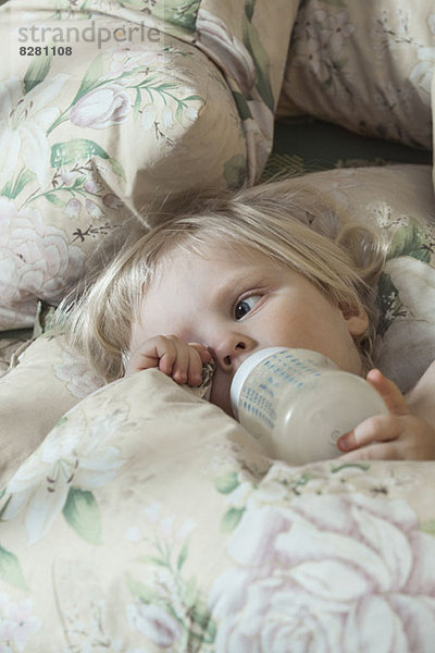 Müde Mädchen auf dem Bett trinken aus der Milchflasche