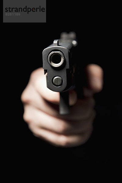 Eine Hand hält eine Waffe und richtet sie auf die Kamera  schwarzer Hintergrund