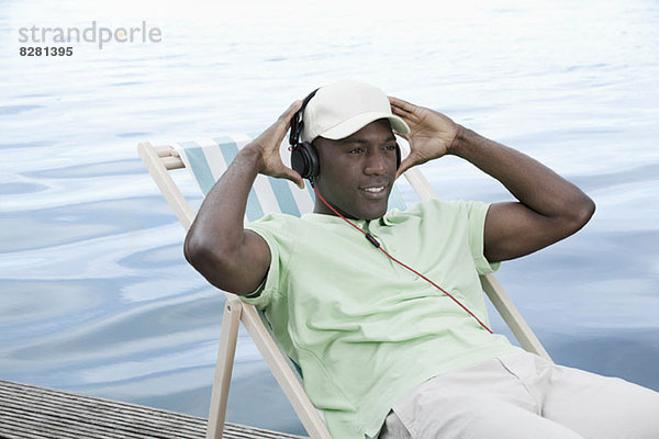 Mann entspannt auf Liegestuhl am See mit Kopfhörer