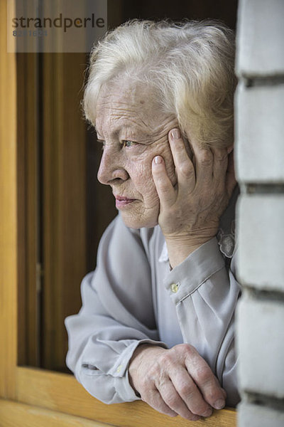 Eine ältere Frau  die sich auf ein Fensterbrett stützt und kontemplativ aussieht.