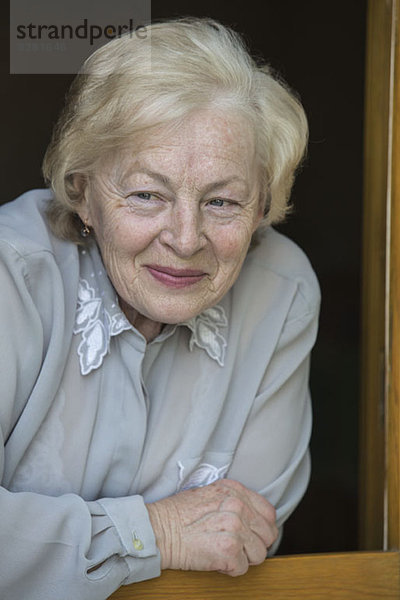 Eine ältere Frau  die sich auf eine Fensterbank stützt und lächelt  während sie wegguckt.