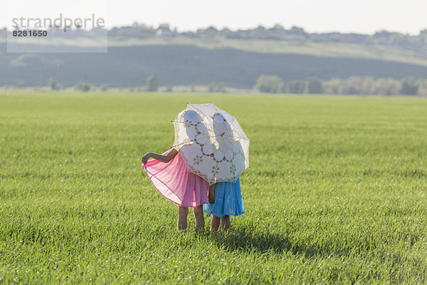 Zwillingsschwestern stehen auf einem sonnigen Feld unter einem Schirm