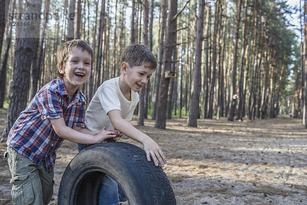Zwei kleine Jungen schieben einen Reifen in einem Waldgebiet.