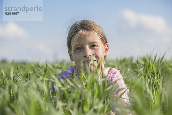 Ein junges lächelndes Mädchen  das an einem Sommertag im Gras liegt.
