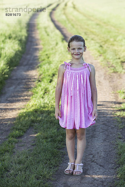 Ein junges lächelndes Mädchen  das auf einem Feldweg auf dem Land steht.