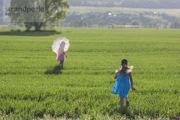 Ein junges Mädchen  das seine Zwillingsschwester im sonnigen Feld einholt.